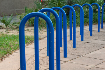 Large blue metal bicycling hub racks. The curved wave shape of the metal stands is attached to the edge of a brick foundation patio. The commercial short term u bike rack for multiple bikes. 