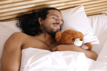 Shirtless long haired man sleeping with teddy bear