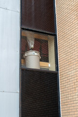 A white bucket sits on a window sill in a commercial brick building. The glass window is closed....