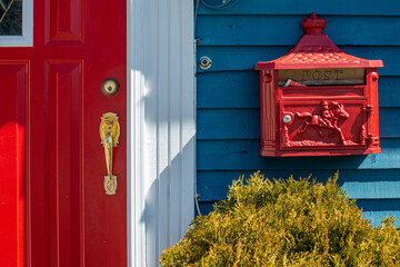 A bright red retro metal mailbox, or letterbox, affixed to the exterior wall of a blue wooden house...