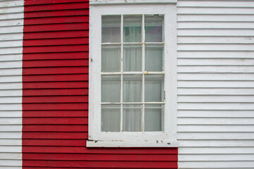 The exterior of a white wooden house wall with a red painted panel, and a closed glass single hung...