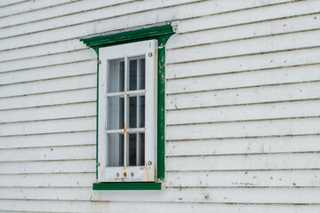 A small single casement window in a white narrow wood beveled clapboard siding exterior wall of a...
