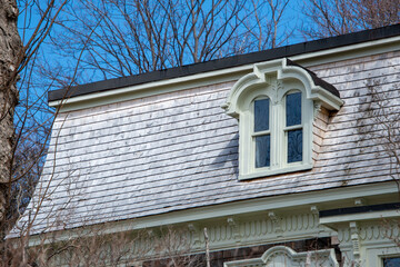 A hip roof of a vintage green wooden building with cream color trim. The house has a double hung...