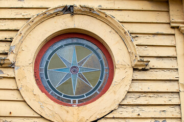Fototapeta na wymiar The exterior of a vintage building with yellow clapboard siding. There's a round window with a stained glass window. A star is in the middle made of blue and green glass. The trim is decorative.