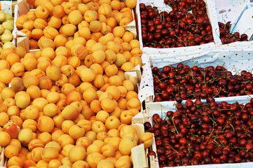 Apricots and cherries in open wooden boxes for sale at the food market.