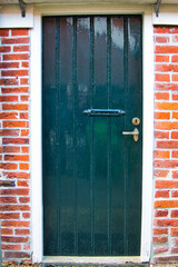 Rustic, dark green wooden door with copper handle in a traditional Dutch farmhouse

