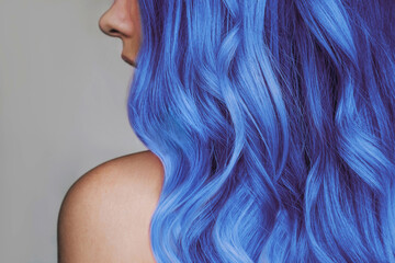 Close-up of the wavy hot blue hair of a young woman isolated on a gray background. Result of coloring, highlighting, perming. Bright saturated extravagant color. Beauty and fashion