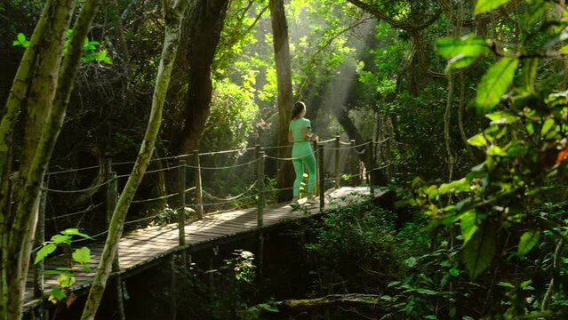 Woman ultra marathon trail runner running in morning forest. a slender athletic woman runs along a wooden bridge in a city park in the morning, the rays of the sun through