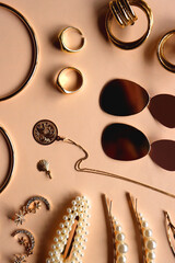 Various gold jewelry and pearl hair clips on peach colored background. Flat lay.