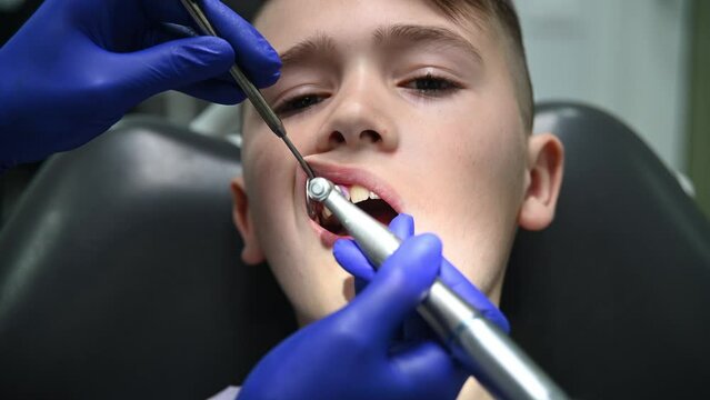 The dentist cleans the boy's teeth with a special device. Front face