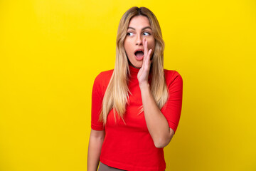 Young Uruguayan woman isolated on yellow background whispering something with surprise gesture while looking to the side
