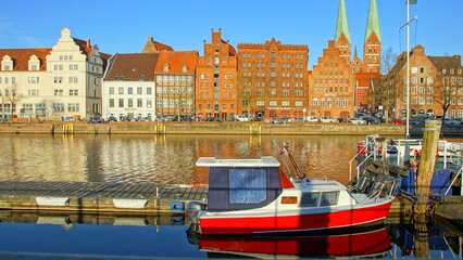 historische Häuserfassaden und Kirchtürme in Lübeck entlang der Trave und rotes Boot im...