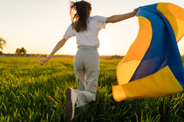 Girl with flag of Ukraine runs across the field close-up and copy space.