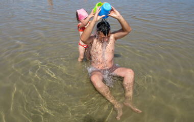 
Image of a dad at the seaside while his daughter throws water on him to cool off from the heat. Beach vacation in Italy