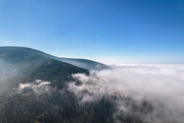 Aerial view of green mountains covered with clouds, clear blue sky. 
