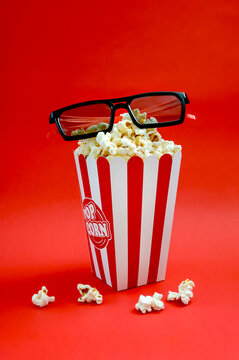 Fresh popcorn in a striped paper cup with 3d glasses on a red background. The concept of cinemas, television, shows. Vertical view