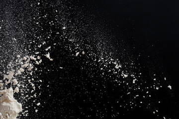 Flying white flour, powder on a black background. Spray of particles, lumps, pieces of white...