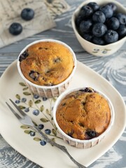 Muffins with blueberry and lavender in rustic style. Cupcakes on the ceramic plate with a pattern of blueberries. Bowl full of blueberry, small fork. Mini cakes on the grey wooden table