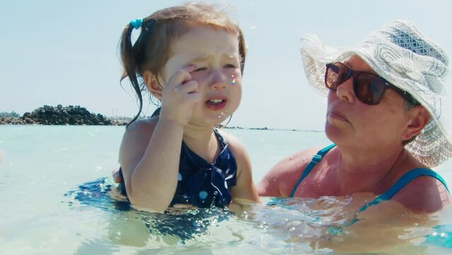Salty water in the eyes. Toddler girls cries and rubs the eye irritated by sea water