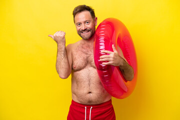 Middle age caucasian man holding inflatable donut isolated on yellow background pointing to the...