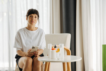 Beautiful young caucasian woman using smartphone shopping online at home with cosmetics and...