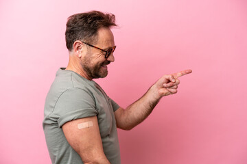 Middle age man wearing a band aids isolated on pink background pointing to the side to present a...