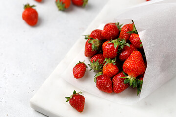 Delicious fresh strawberries wrapped in a paper bag on marble board and grey background. Berry take away. Place for text