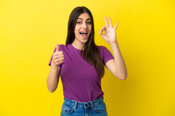 Young caucasian woman isolated on yellow background showing ok sign and thumb up gesture