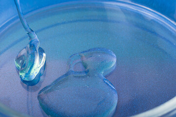 Closeup photography of dripping cosmetic gel in petri dish.Blue background.