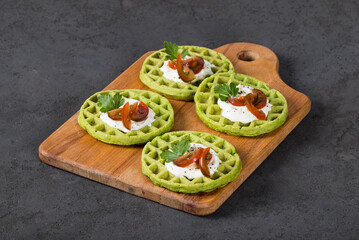 Round spinach waffles with cottage cheese, cherry tomatoes and parsley, on a wooden board. Dark gray background
