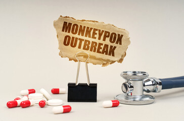 Near the stethoscope are pills and a clip with a cardboard sign - Monkeypox outbreak