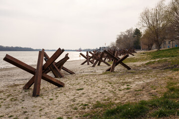 Metallic military obstacles, anti tank hedgehoges on bank. Constructions protecting freedom, independence of Ukraine 2022