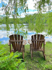 Chaises Adirondack en bois dans un jardin sur le bord de l'eau. Paysage d'été au travers les feuilles vertes retombantes d'un arbre. Chaise de patio sous un Saule pleureur