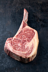 Raw dry aged Wagyu tomahawk steak offered as close-up on an old rustic board
