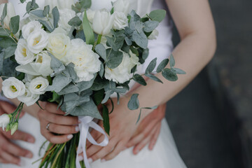 The bride in a lacy white dress holds a bouquet. Close up of bride's bouquet of white flowers. The bride and groom embrace.