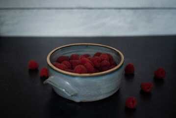 Bowl of raspberries in blue handmade ceramic bowl on dark background 