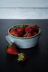 Bowl of raspberries in blue handmade ceramic bowl on dark background 