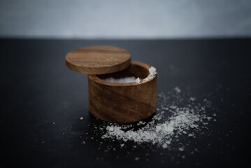 Side view of sea salt on dark moody background inside wooden salt container.