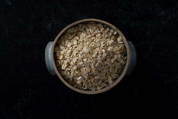 Top view of handmade ceramic bowl of organic oats on dark moody background.