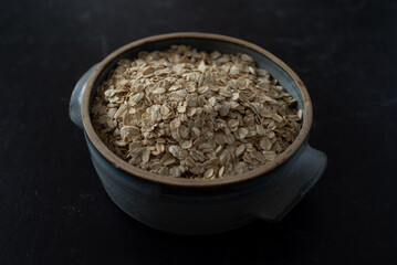 Closeup top view of handmade ceramic bowl of organic oats on dark moody background.