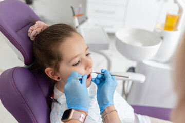 Close-up of pretty little girl opening his mouth wide during treating her teeth by the dentist