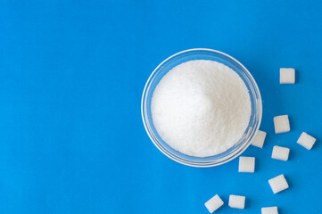 Heap of white granulated sugar with sugar cube on blue background