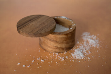 Top and side and angled view of sea salt on orange terracotta background inside round wooden salt container.