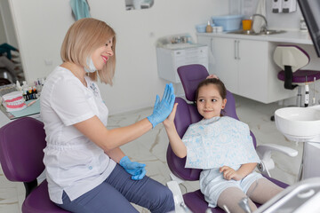 A child is happy after dental treatment and giving high-five to his doctor in a modern white dental clinic.