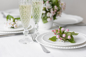 Beautiful table decor for a wedding dinner with a spring blooming apple tree flowers. Celebration of a special event. Fancy white plates, wineglasses