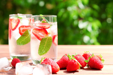 Two glasses of fresh strawberry lemonade with ice and mint against greenery. Summer refreshment...