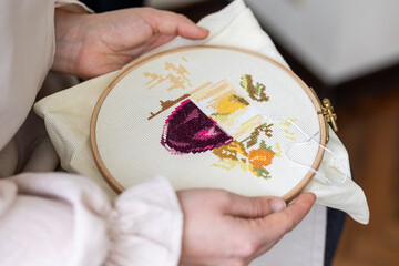 Cross-stitch embroidering in progress. Young girl in linen clothes is doing handmade embroidery