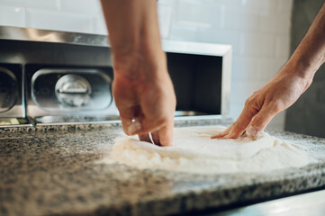 Kitchen chef preparing dough for pizza while working in a pizza place