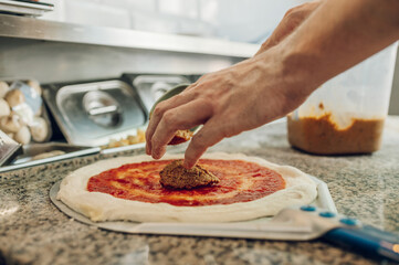 Man worker in a pizza place placing ingredients on pizza dough