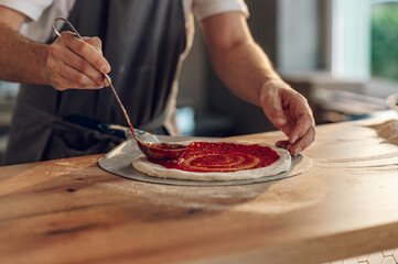 Man worker in a pizza place placing ingredients on pizza dough